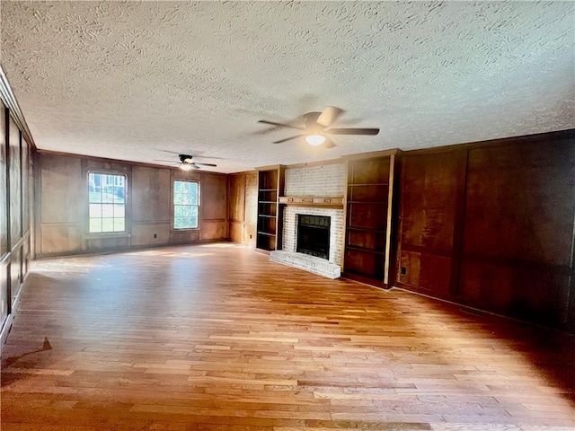 unfurnished living room featuring built in features, ceiling fan, light hardwood / wood-style floors, a brick fireplace, and a textured ceiling