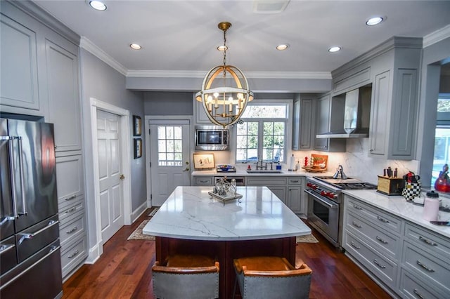 kitchen featuring high quality appliances, a center island, gray cabinetry, decorative light fixtures, and wall chimney exhaust hood