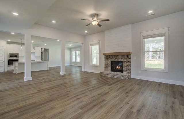 unfurnished living room featuring ceiling fan, plenty of natural light, dark hardwood / wood-style floors, and a brick fireplace