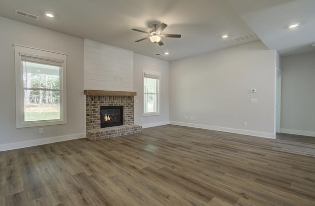 unfurnished living room featuring plenty of natural light, ceiling fan, dark hardwood / wood-style flooring, and a brick fireplace