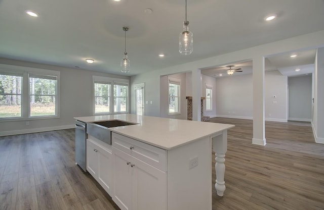 kitchen featuring ceiling fan, pendant lighting, a center island with sink, hardwood / wood-style flooring, and white cabinetry