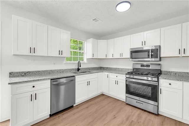 1645 Cobbs Creek Ln, Decatur, GA 30032 - kitchen with stainless steel appliances, a sink, white cabinets, light wood-type flooring, and a textured ceiling