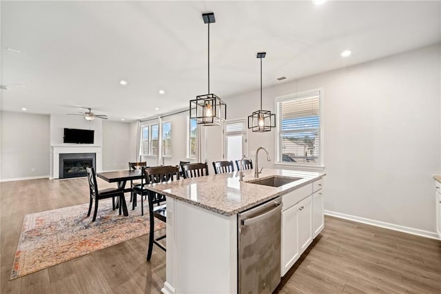 kitchen featuring a glass covered fireplace, a kitchen island with sink, light wood-type flooring, stainless steel dishwasher, and a sink