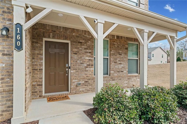 view of exterior entry featuring a porch and brick siding