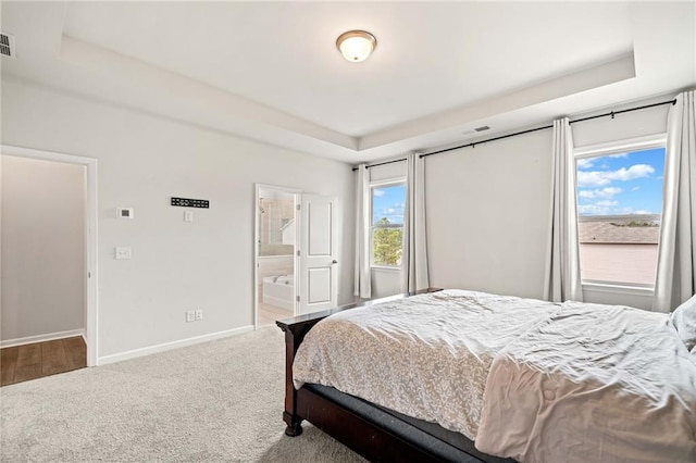 bedroom featuring baseboards, visible vents, ensuite bath, a tray ceiling, and carpet floors