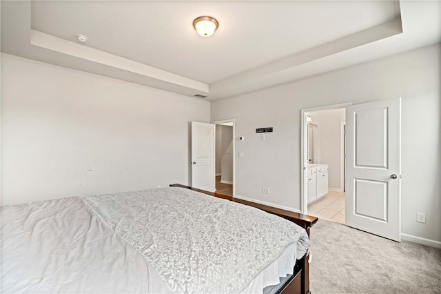 bedroom featuring ensuite bath, a raised ceiling, visible vents, and baseboards