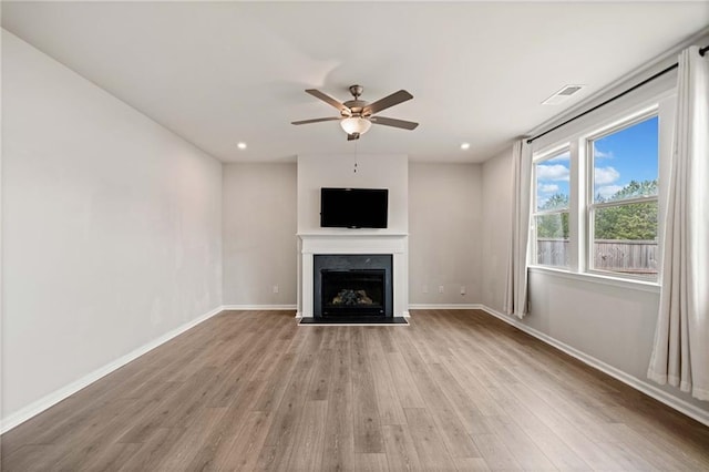 unfurnished living room with ceiling fan, light wood-style flooring, a fireplace, visible vents, and baseboards