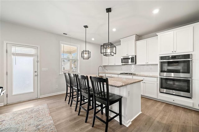 kitchen featuring an island with sink, light wood-style floors, tasteful backsplash, and appliances with stainless steel finishes