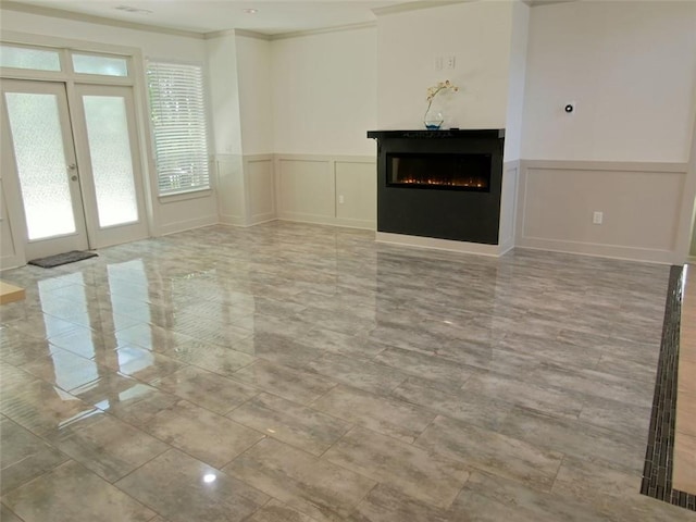 4590 River Stone Trl, Douglasville, GA 30135 - unfurnished living room featuring a lit fireplace, a decorative wall, a wainscoted wall, crown molding, and french doors