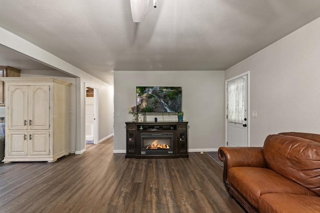 living room featuring a ceiling fan, dark wood-style flooring, baseboards, and a glass covered fireplace