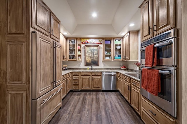 kitchen featuring glass insert cabinets, a sink, light stone countertops, a raised ceiling, and appliances with stainless steel finishes
