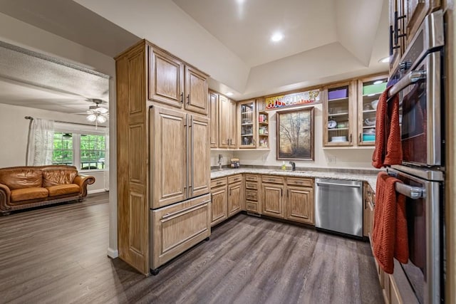 kitchen featuring light stone countertops, glass insert cabinets, a sink, stainless steel appliances, and dark wood-style floors