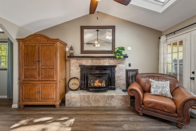 sitting room with a fireplace, ceiling fan, lofted ceiling with skylight, and dark wood-style floors
