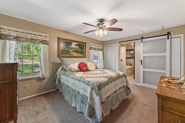 carpeted bedroom with ensuite bathroom, a textured ceiling, a barn door, visible vents, and baseboards