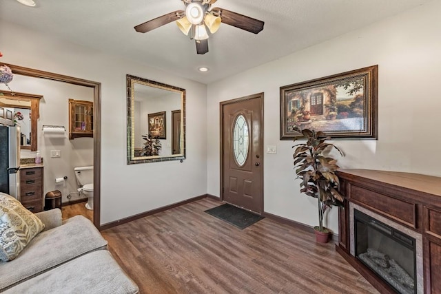 entryway featuring a ceiling fan, recessed lighting, baseboards, dark wood-style flooring, and a glass covered fireplace