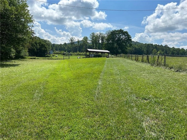view of yard with fence, a rural view, and a view of trees