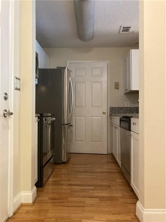 1075 Peachtree Walk Unit A205, Atlanta, GA 30309 - kitchen with appliances with stainless steel finishes, light wood-style floors, white cabinets, and a textured ceiling