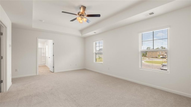 empty room featuring light colored carpet, a ceiling fan, baseboards, and a raised ceiling