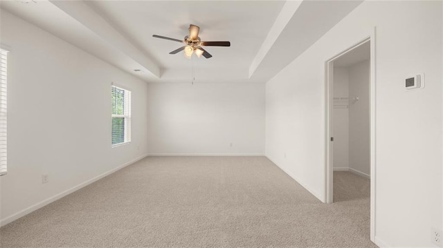 unfurnished room with light colored carpet, a raised ceiling, ceiling fan, and baseboards