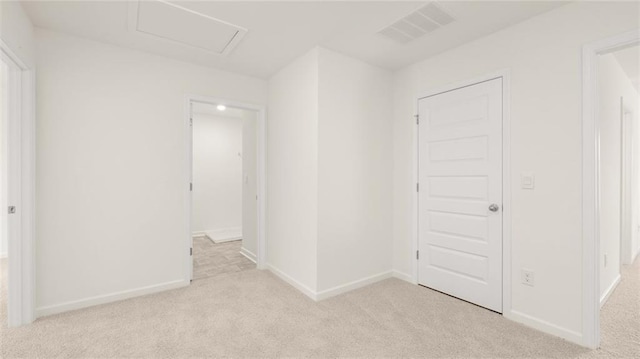 carpeted empty room with attic access and baseboards