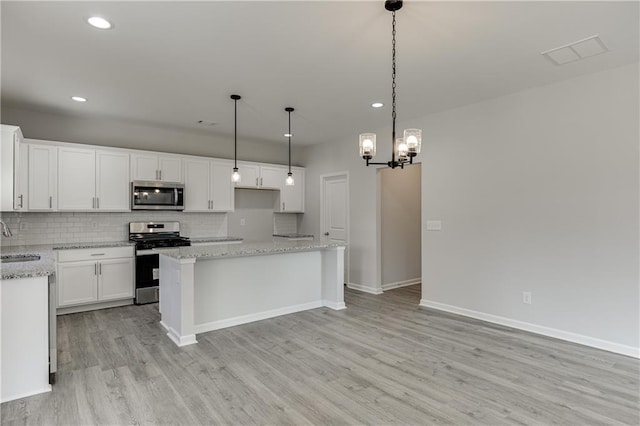 kitchen featuring white cabinets, a sink, stainless steel appliances, light wood-style floors, and backsplash