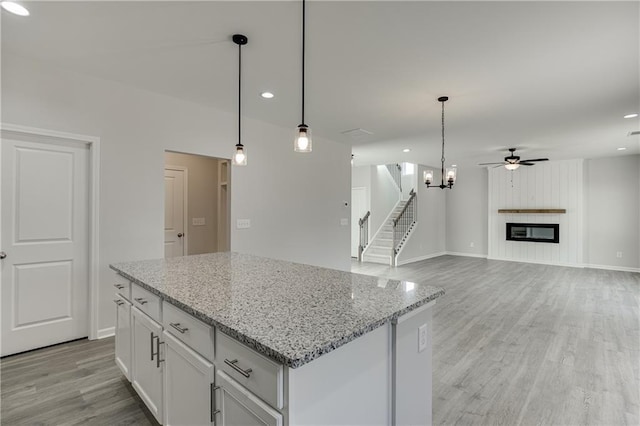 kitchen featuring a large fireplace, ceiling fan with notable chandelier, light wood-style flooring, and white cabinets