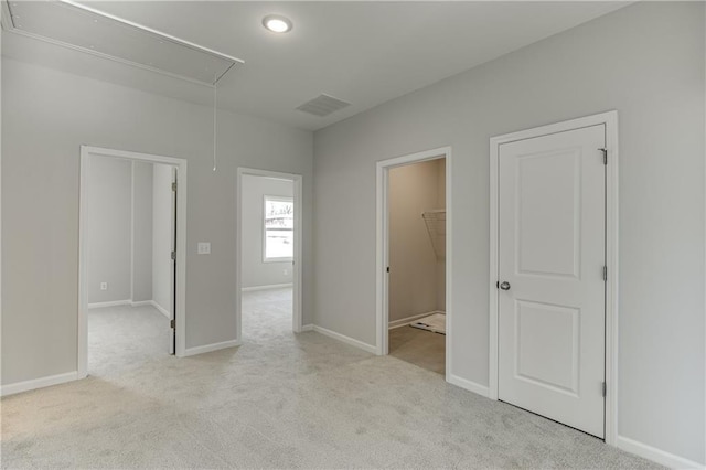 unfurnished bedroom featuring a walk in closet, visible vents, attic access, carpet flooring, and baseboards