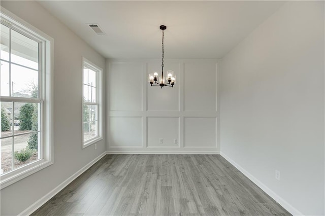 unfurnished dining area featuring plenty of natural light, an inviting chandelier, visible vents, and a decorative wall