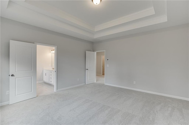 unfurnished bedroom featuring light carpet, baseboards, ornamental molding, a tray ceiling, and ensuite bath