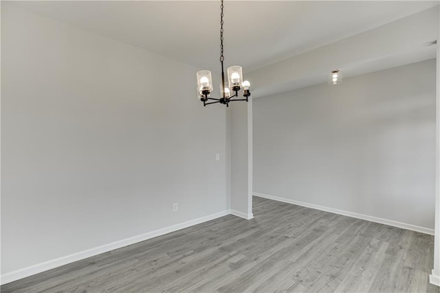 empty room featuring an inviting chandelier, wood finished floors, and baseboards