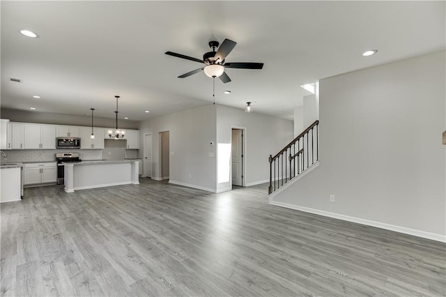 unfurnished living room with a ceiling fan, light wood-style flooring, stairway, and baseboards