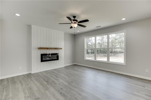 unfurnished living room with ceiling fan, a large fireplace, wood finished floors, visible vents, and baseboards