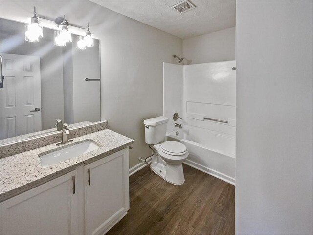 full bathroom with hardwood / wood-style floors, vanity, a textured ceiling, shower / washtub combination, and toilet