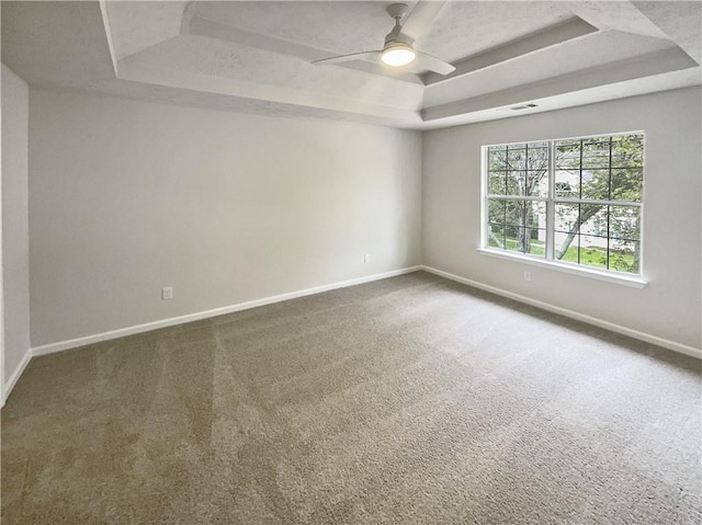 spare room with a raised ceiling, carpet flooring, and ceiling fan