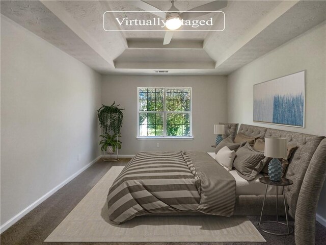 carpeted bedroom with ceiling fan and a raised ceiling