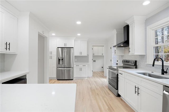 kitchen featuring white cabinetry, sink, stainless steel appliances, light wood-type flooring, and wall chimney exhaust hood