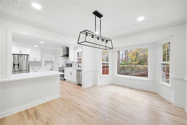 kitchen featuring appliances with stainless steel finishes, pendant lighting, sink, white cabinets, and wall chimney range hood