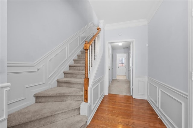 staircase featuring a decorative wall, crown molding, a wainscoted wall, and wood finished floors