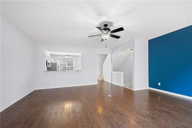 unfurnished living room featuring ceiling fan with notable chandelier, baseboards, and wood-type flooring