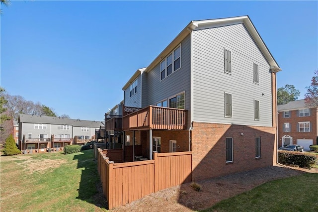 rear view of house featuring a deck, a yard, fence, and brick siding