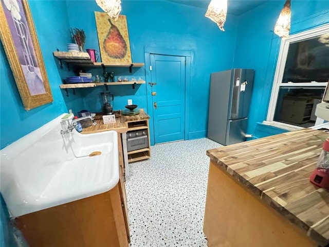 kitchen featuring a sink, speckled floor, wooden counters, and freestanding refrigerator