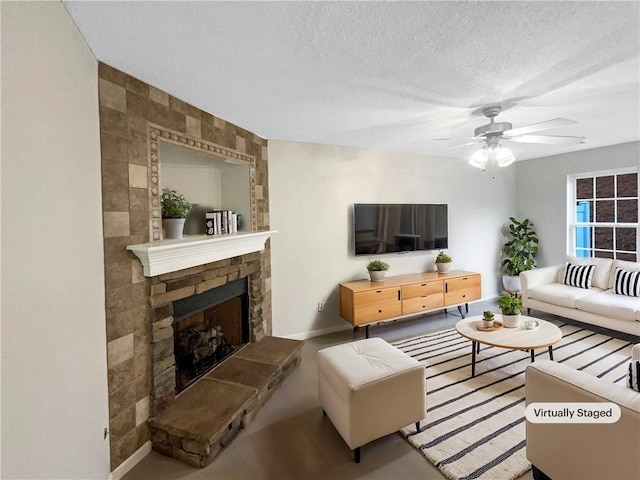 living room featuring baseboards, a ceiling fan, a textured ceiling, and a stone fireplace