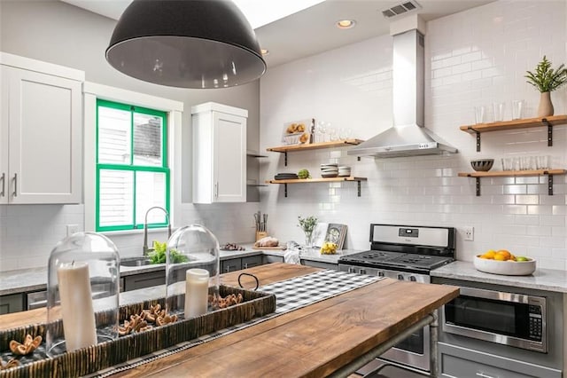 kitchen with wall chimney exhaust hood, butcher block counters, white cabinetry, and stainless steel appliances