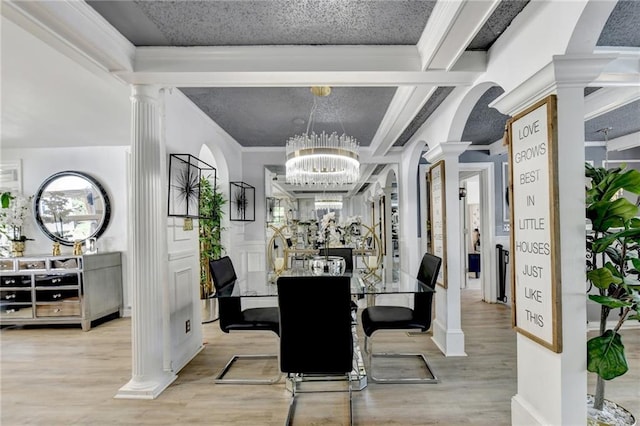 dining space with an inviting chandelier, ornamental molding, light wood-type flooring, and decorative columns