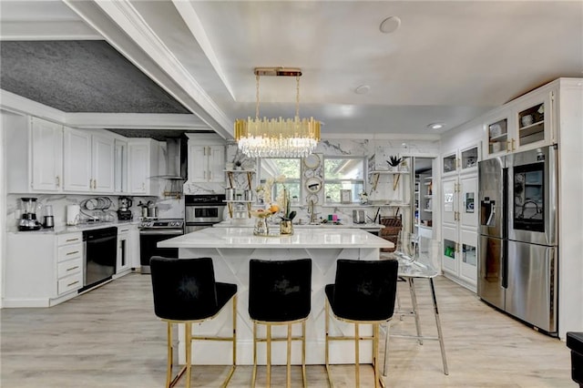 kitchen featuring wall chimney exhaust hood, stainless steel appliances, a center island, decorative light fixtures, and white cabinetry