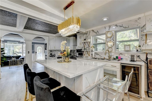 kitchen with sink, a kitchen island, hanging light fixtures, beverage cooler, and light hardwood / wood-style flooring