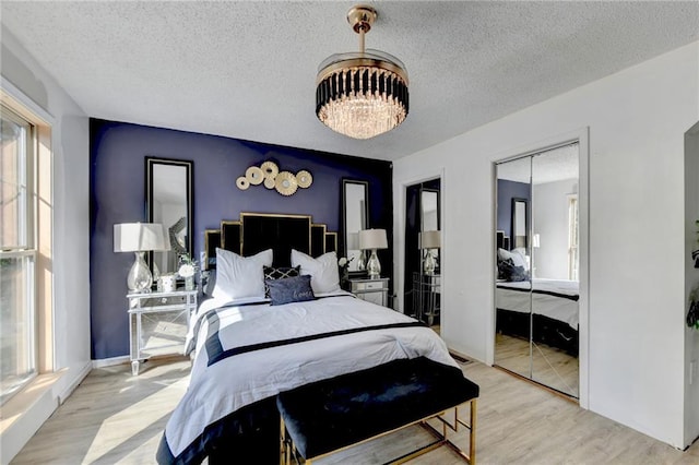 bedroom with a textured ceiling, multiple closets, and light hardwood / wood-style flooring