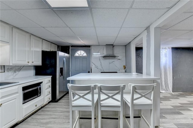 kitchen featuring white cabinets, a breakfast bar, light hardwood / wood-style flooring, stainless steel appliances, and ventilation hood