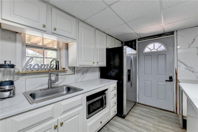 kitchen with appliances with stainless steel finishes, sink, a drop ceiling, backsplash, and white cabinetry