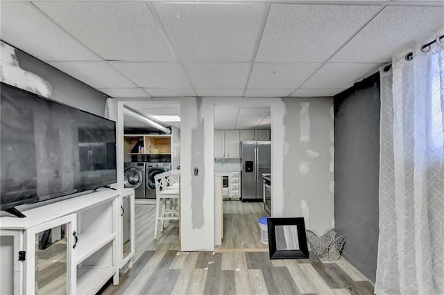 interior space with a paneled ceiling, washing machine and dryer, light wood-type flooring, and stainless steel fridge